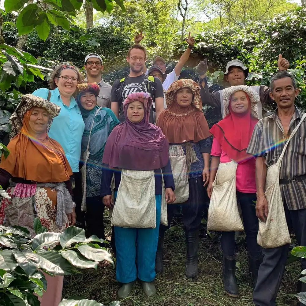 Grupa rolników z kooperatywy Ketiara i odwiedzający ich przedstawiciele palarni JAVA Coffee – wspólne zdjęcie na plantacji wśród krzewów kawowca w Indonezji.