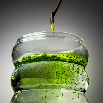 YŌKIRO Matcha Superior – ceremonialna matcha rozpuszczająca się w wodzie, intensywnie zielony proszek tworzący naturalną zawiesinę w szklanym naczyniu, etap przygotowania premium matchy.
